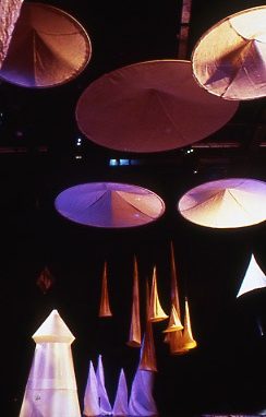 circular and cone shaped objects made from coloured fabric on the floor and hang from above a stage set.