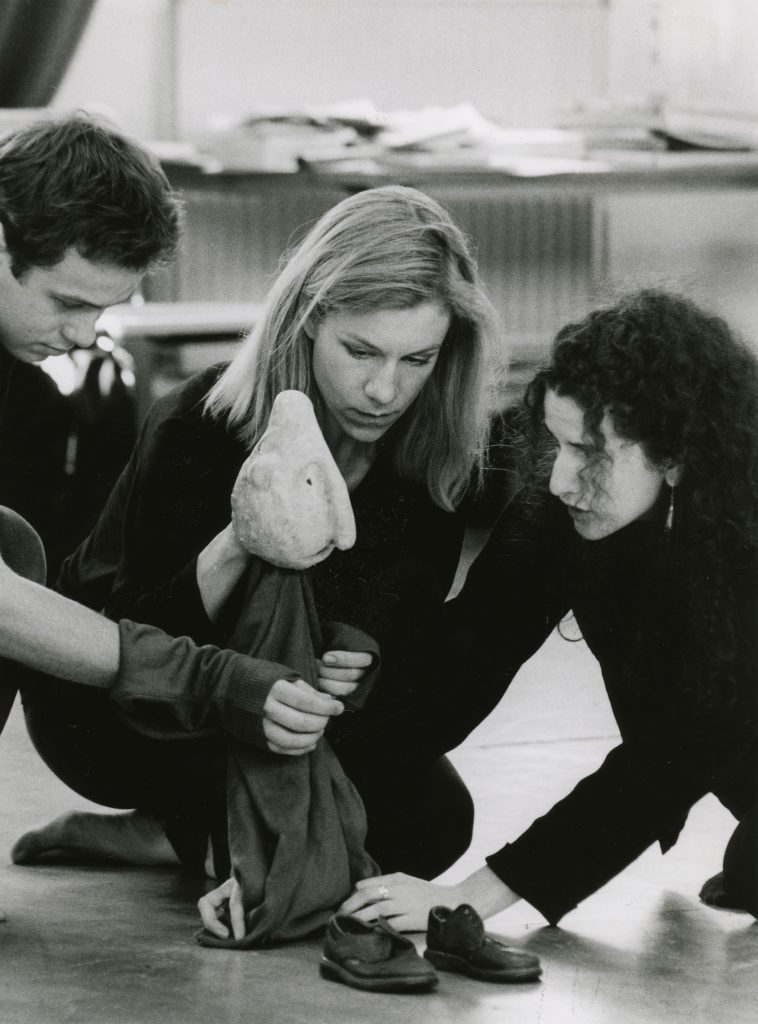 An image from early 1990s. Actress Juliette Stevenson in the middle of the picture and a young actor on the left are being taught how to manipulate a small puppet made of papier mache by Sue Buckmaster who appears with long brown hair on the right hand side of the image.