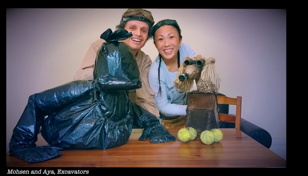 Two performers manipulate a puppet made from black bin bags and a dog made from discarded household items of rubbish.