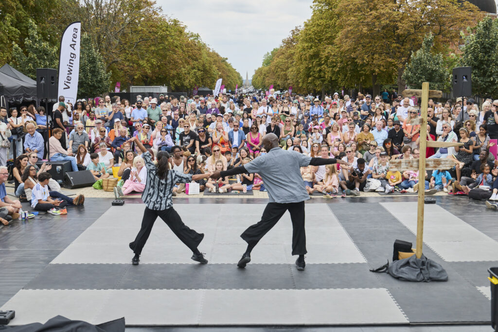 Two dancers with their back to the camera hold hands and as a large crowd looks on in happiness