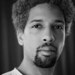 a close up of a man's face with short Afro hair, a moustache and beard